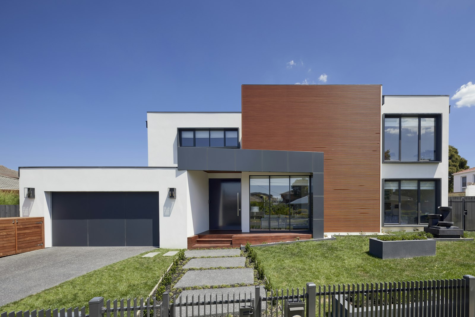 Modern house with white stucco, wood accent panels, and a dark garage door